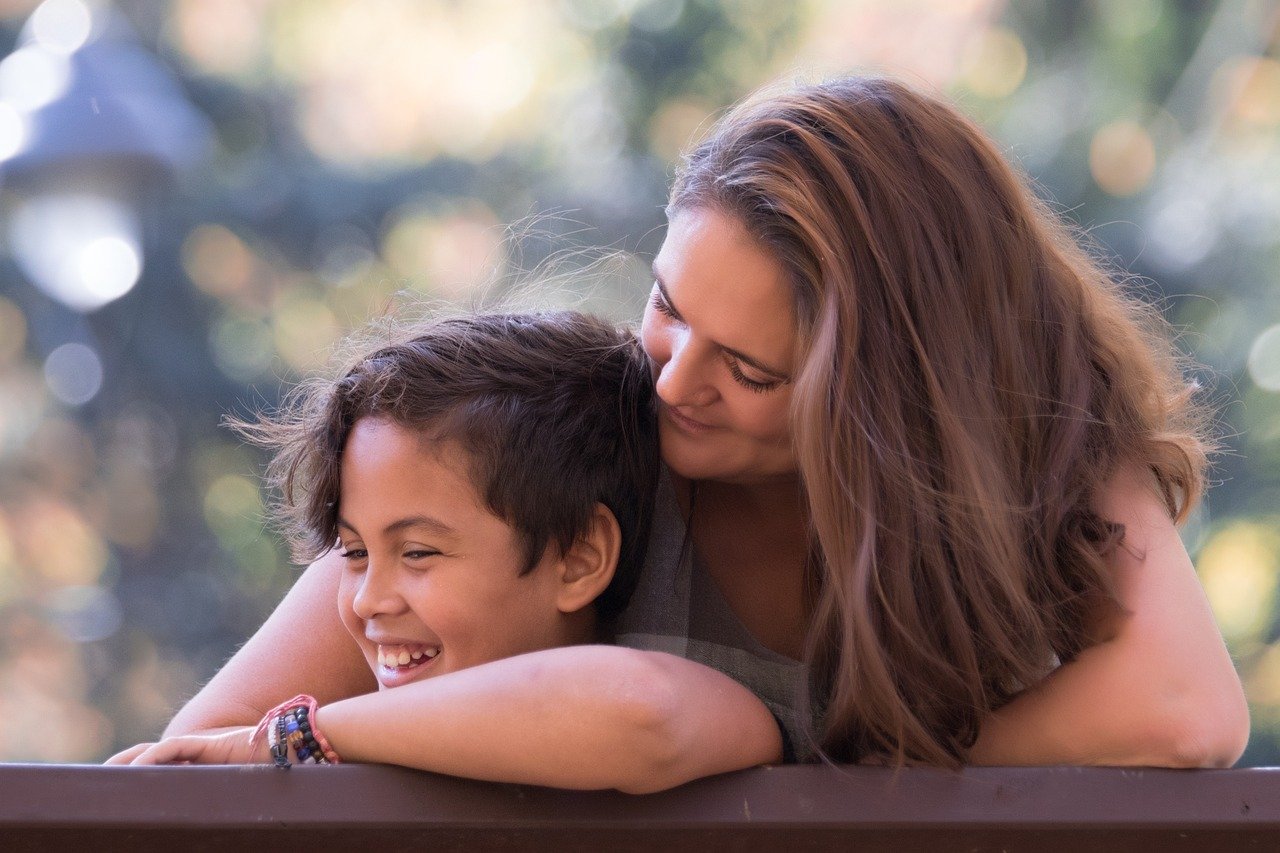 A mother leaning over her smiling son as they laugh together outdoors