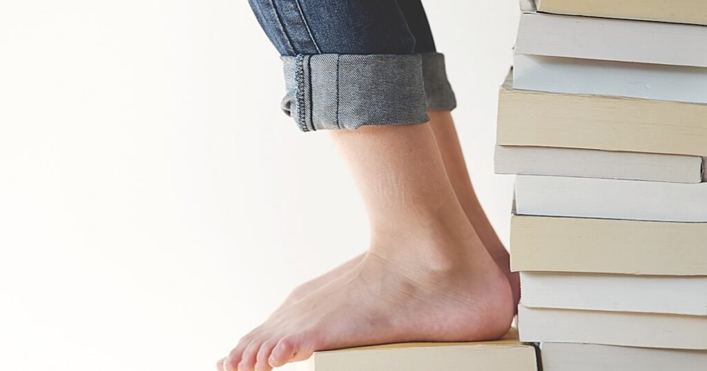 A person sitting on a stack of books while reading, representing self-improvement through reading