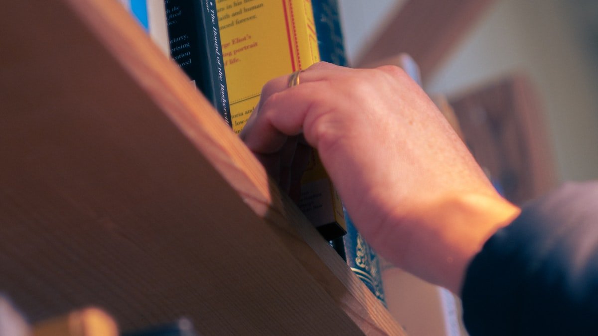 A person reaching for and choosing a book from a bookshelf