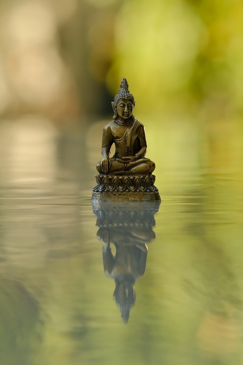 A small bronze Buddha statue reflected in still water, symbolizing mindfulness and calm.