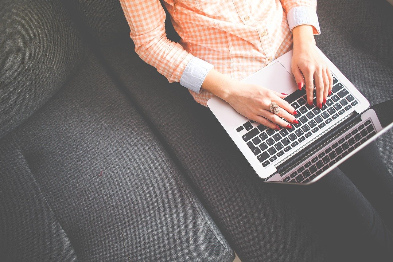A student typing on a laptop with a notebook open beside it, taking notes during an online course.